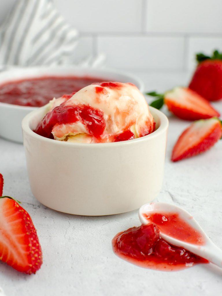 Strawberry sauce over ice cream with fresh strawberries nearby