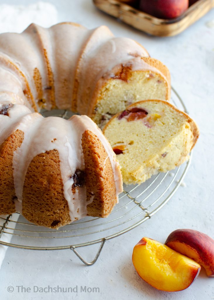 Glazed peach pound cake sliced on a cooling rack with fresh peaches nearby