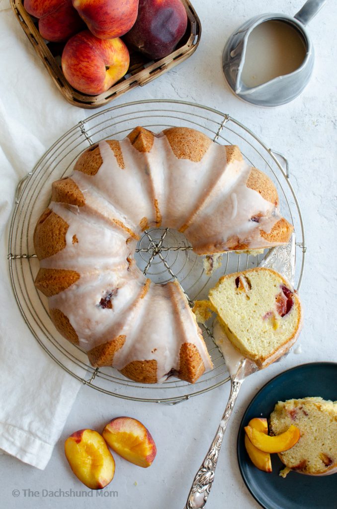 Glazed peach pound cake served on a plate next to cooling rack alongside extra glaze.