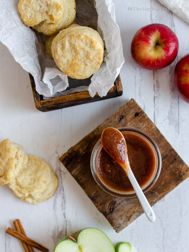 Homemade apple butter on a table with homemade biscuits and fresh apples