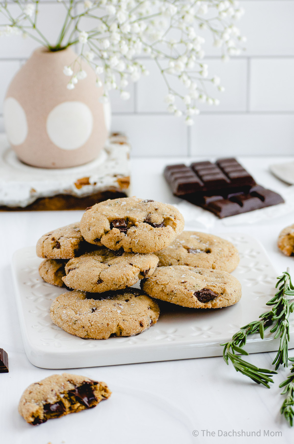 A plate of cookies with dark chocolate chips and fresh rosemary.